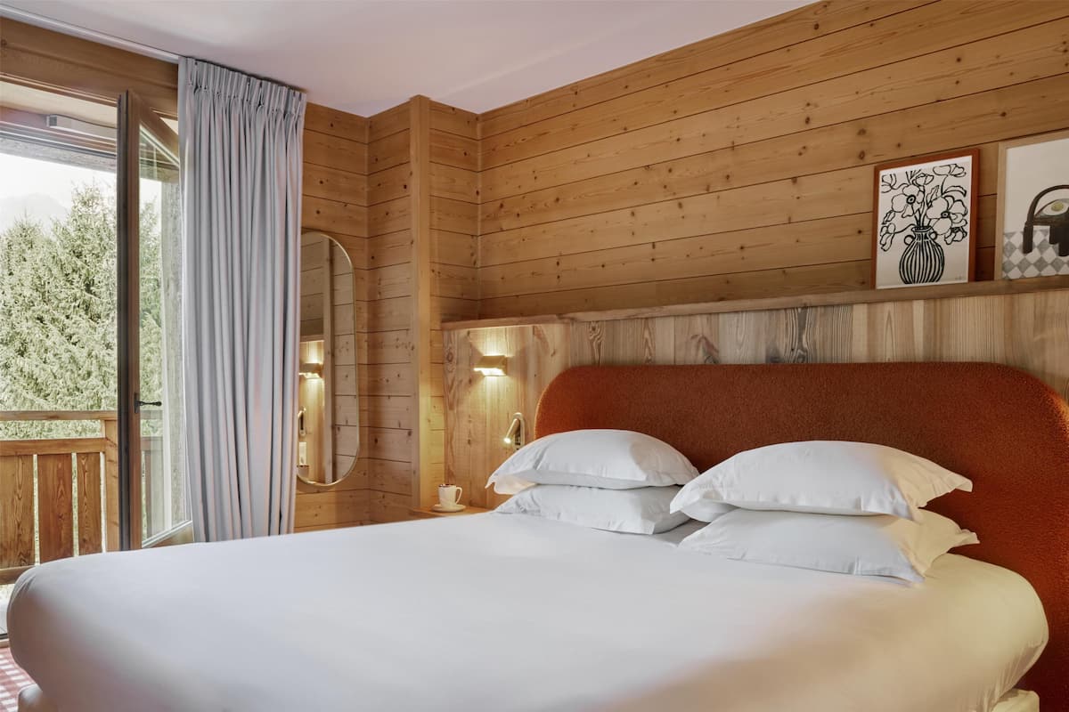 A wooden-paneled room with a bed, a nightstand, a mirror, and framed artwork on the wall.