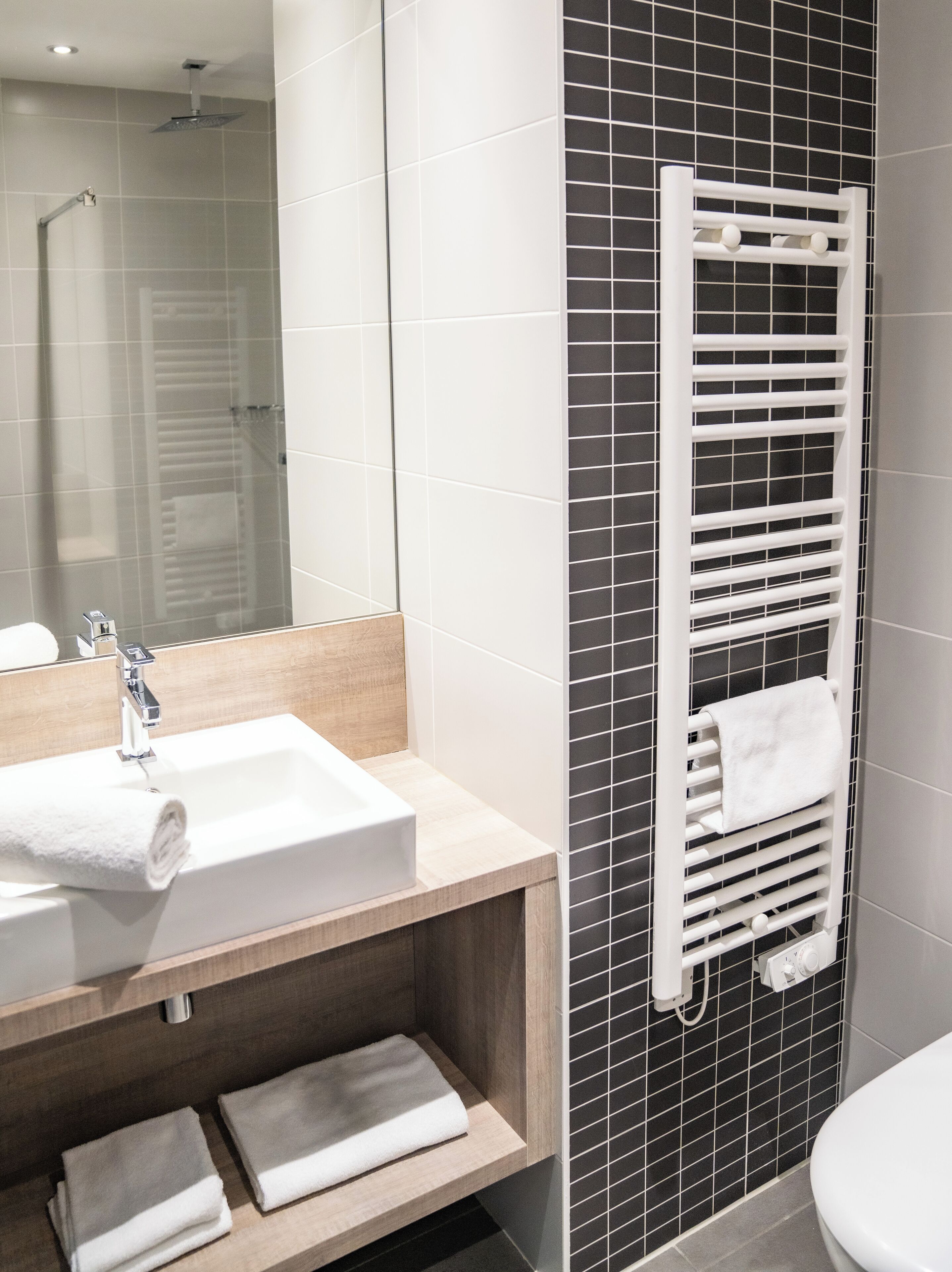A modern bathroom with a white sink, mirror, and a towel rack with towels.