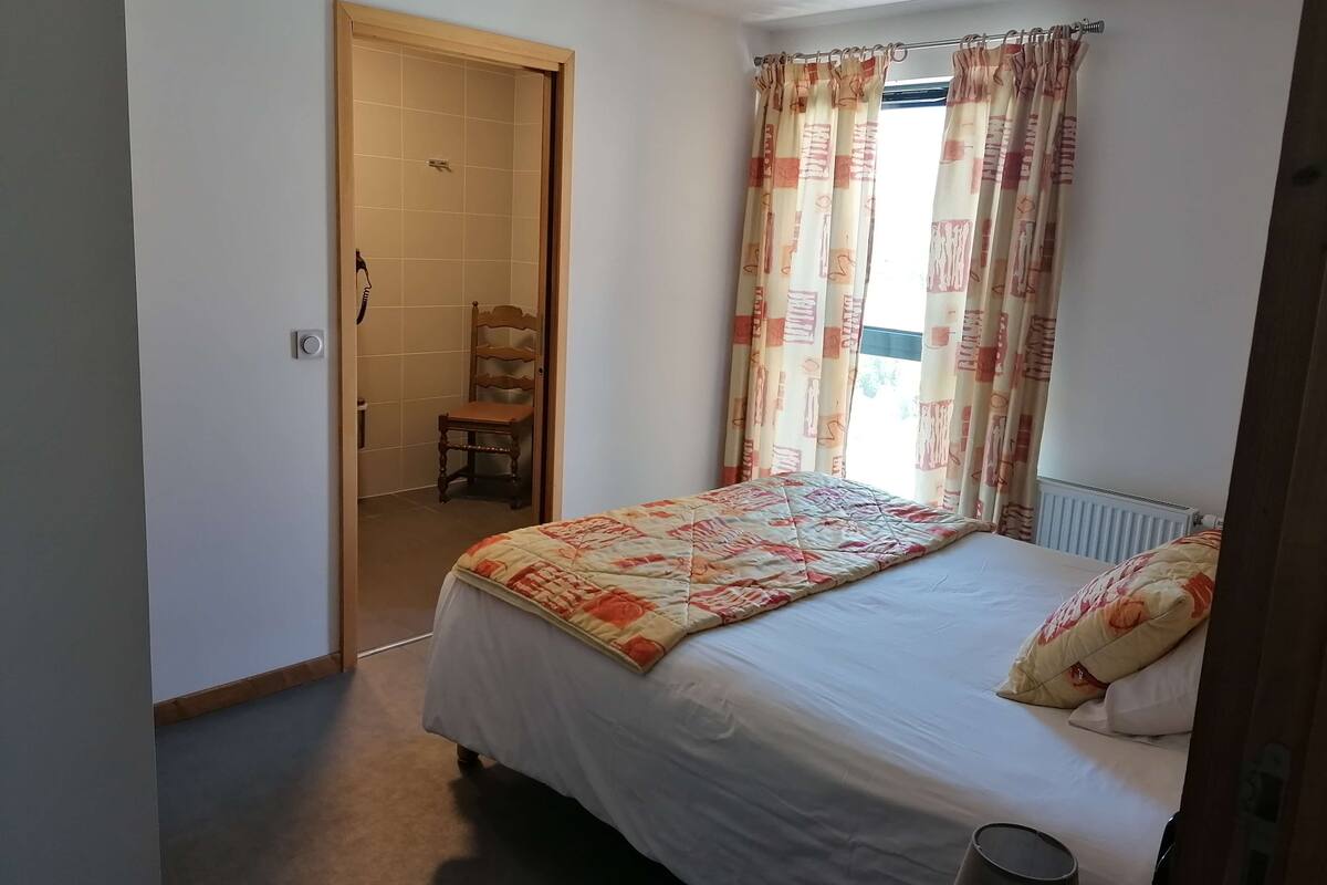 A bedroom with a bed, a chair, a radiator, and a window with curtains.