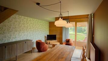 Een moderne woonkamer met een houten eettafel, twee banken, een televisie en een balkon met uitzicht op groen.