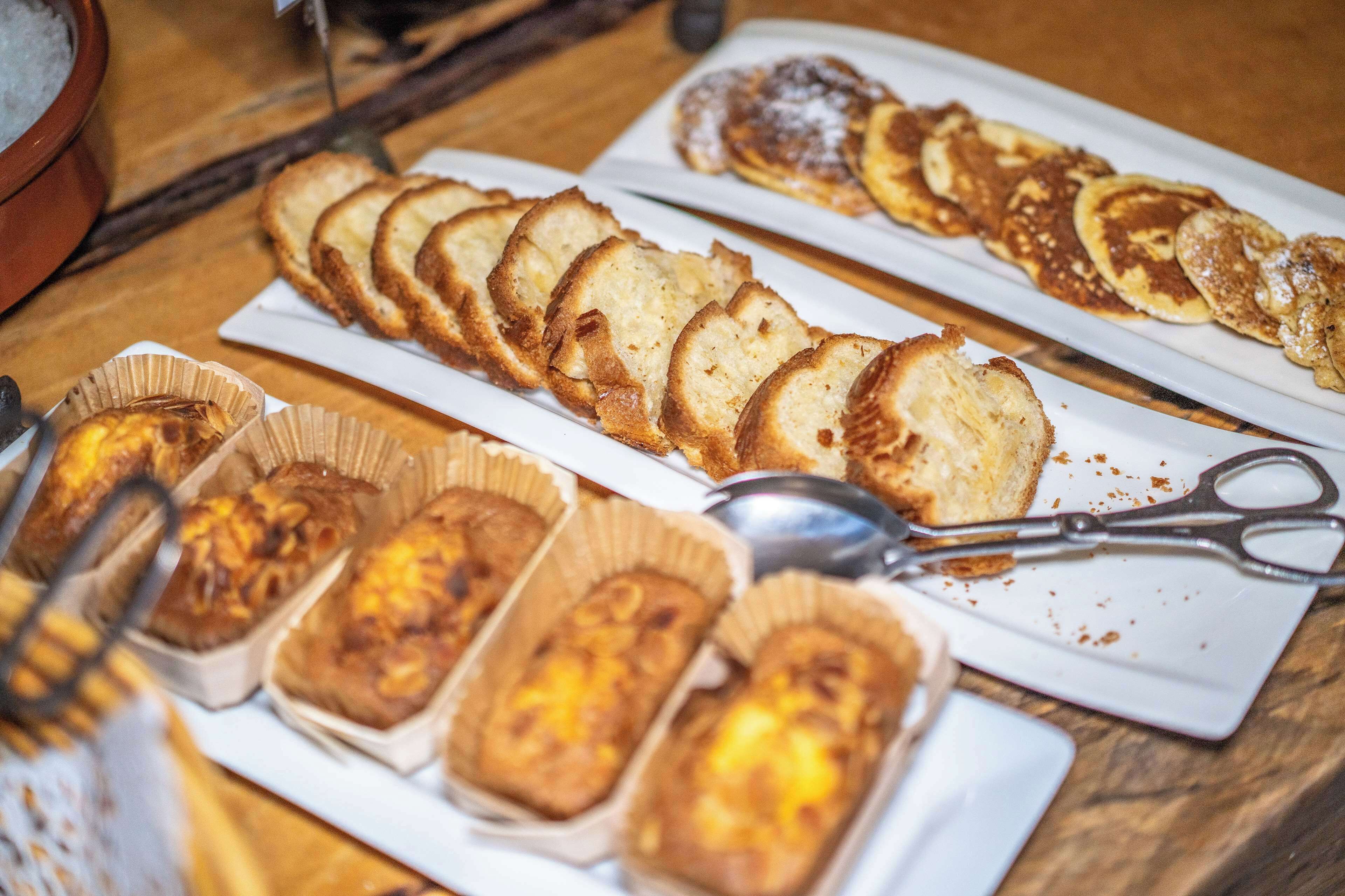 A variety of baked goods on plates, including bread and pastries, with a pair of scissors and a spoon on a wooden table.