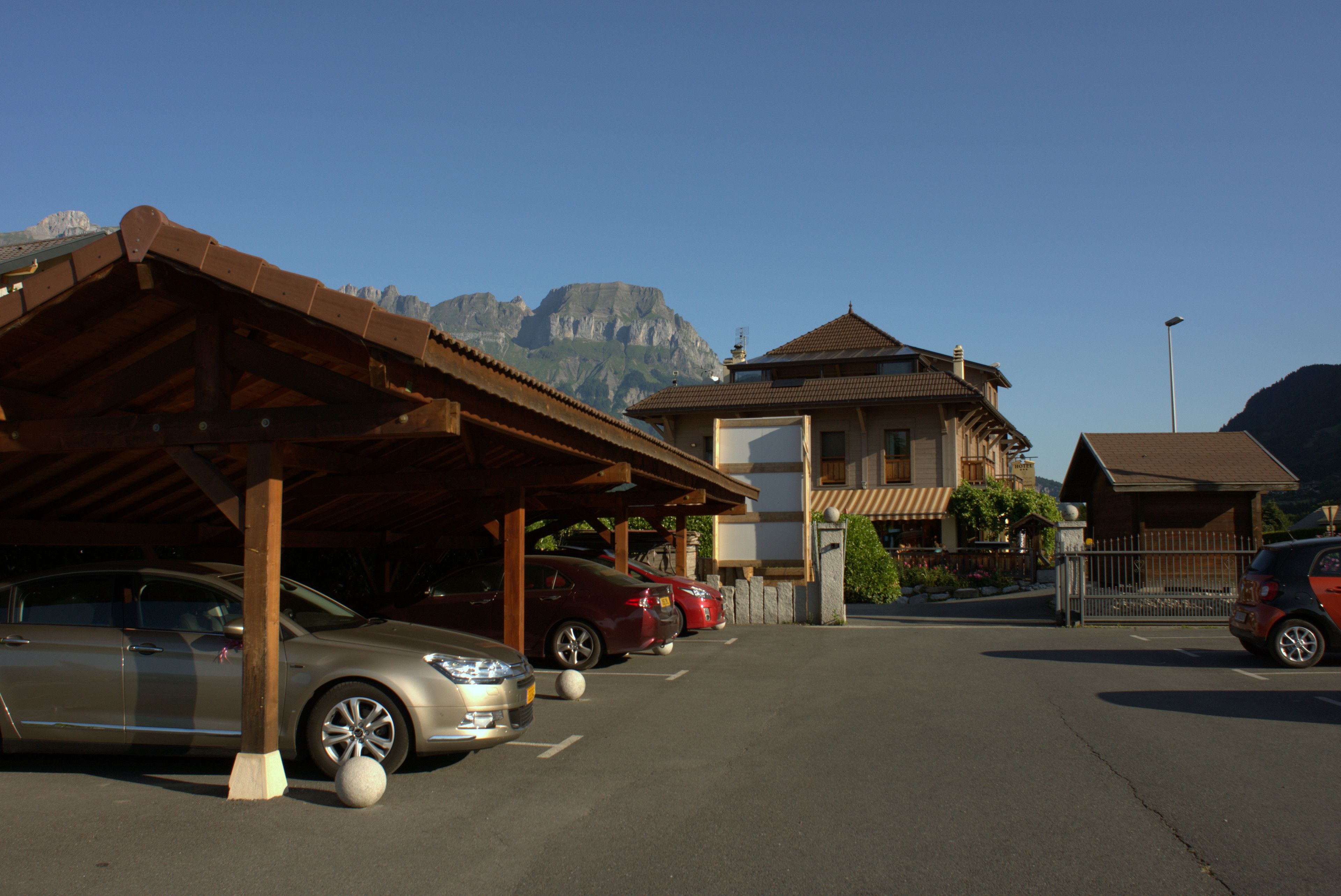 A parking area with cars, a building with a sloped roof, and mountains in the background.