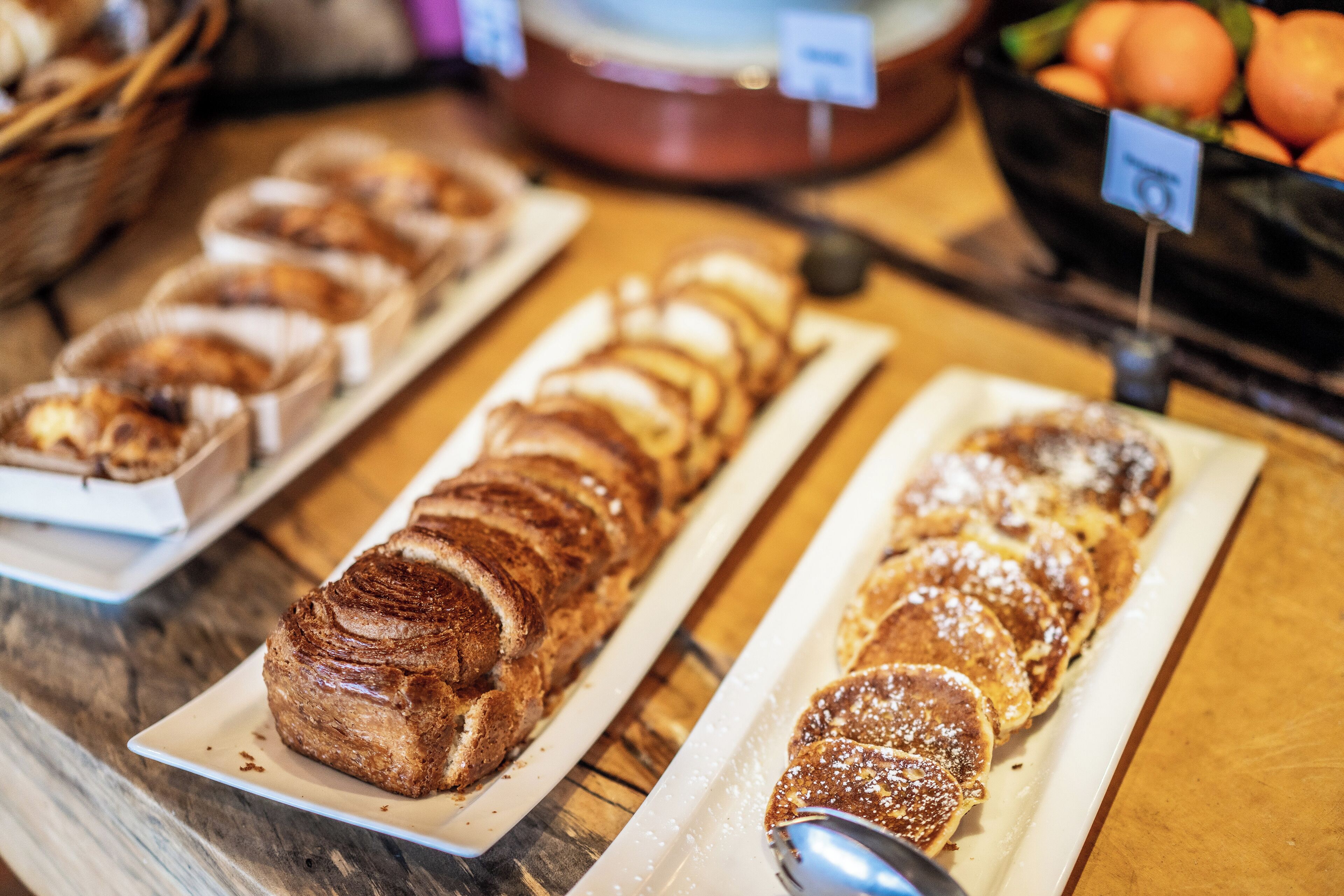 Una vitrina de panadería con diversos pasteles y panes sobre bandejas blancas.