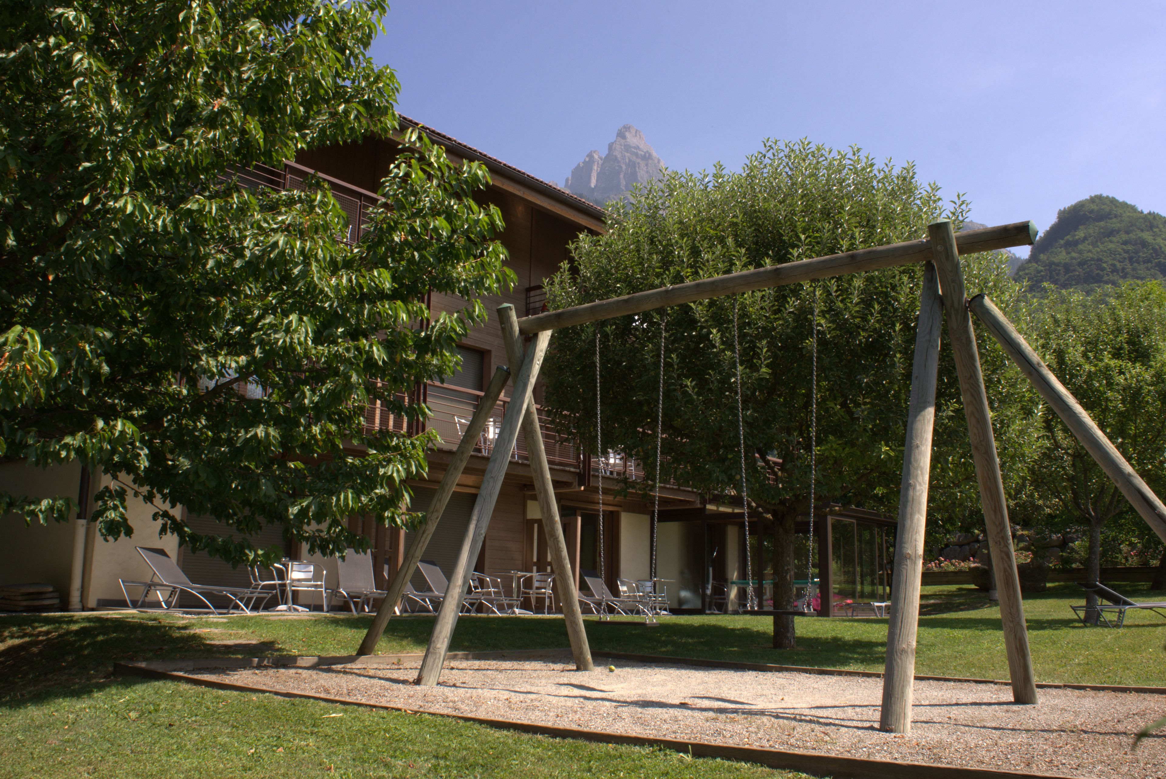 A wooden swing set in a park area with a building in the background.