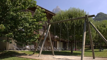 A wooden swing set in a park area with a building in the background.