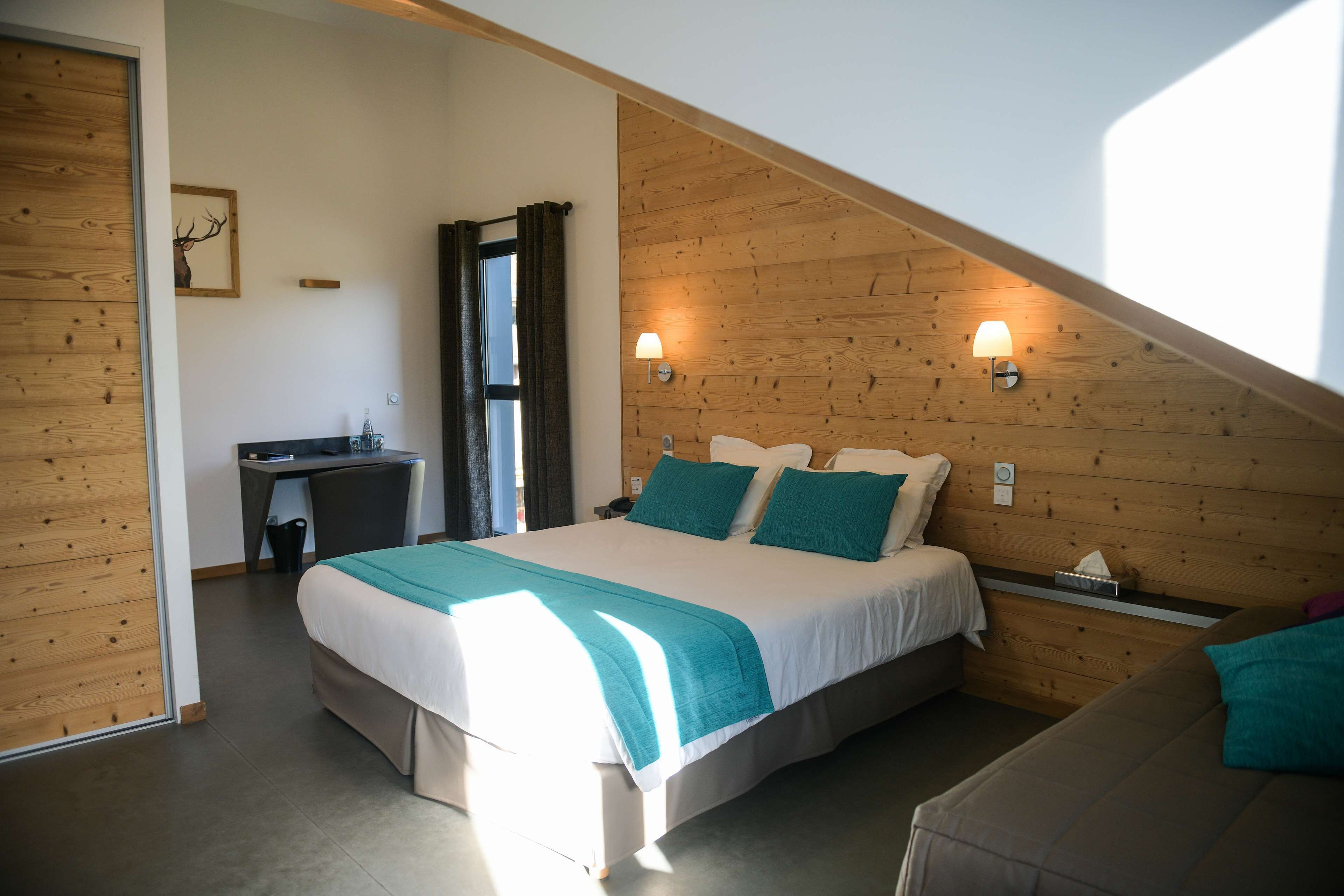 Un dormitorio con una cama grande, un escritorio y una silla. Hay una ventana con cortinas, una lámpara de pared y un techo de madera.