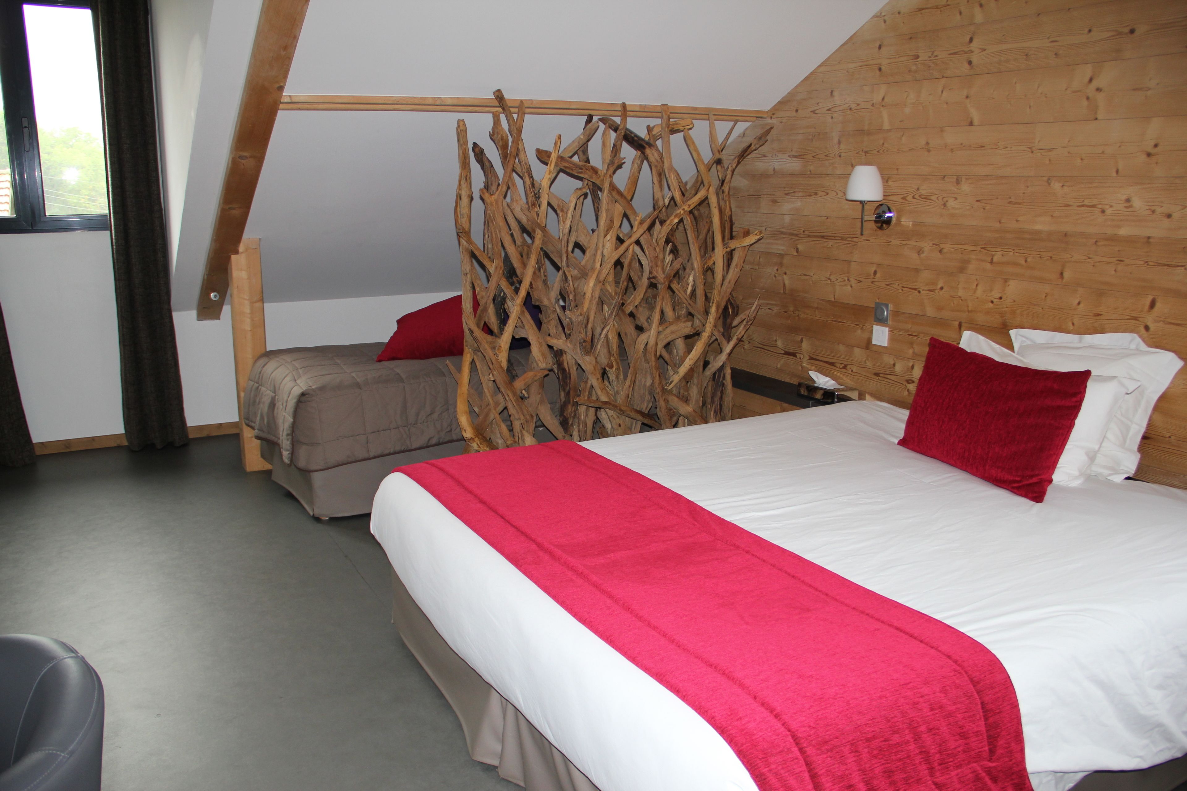 Un dormitorio con literas, una cama grande con una colcha roja, paneles de madera en la pared, una ventana con cortinas y una lámpara de noche.