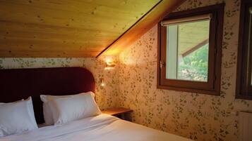 A bedroom with a wooden ceiling, floral wallpaper, a large bed with white bedding, a nightstand, and a window with a view.