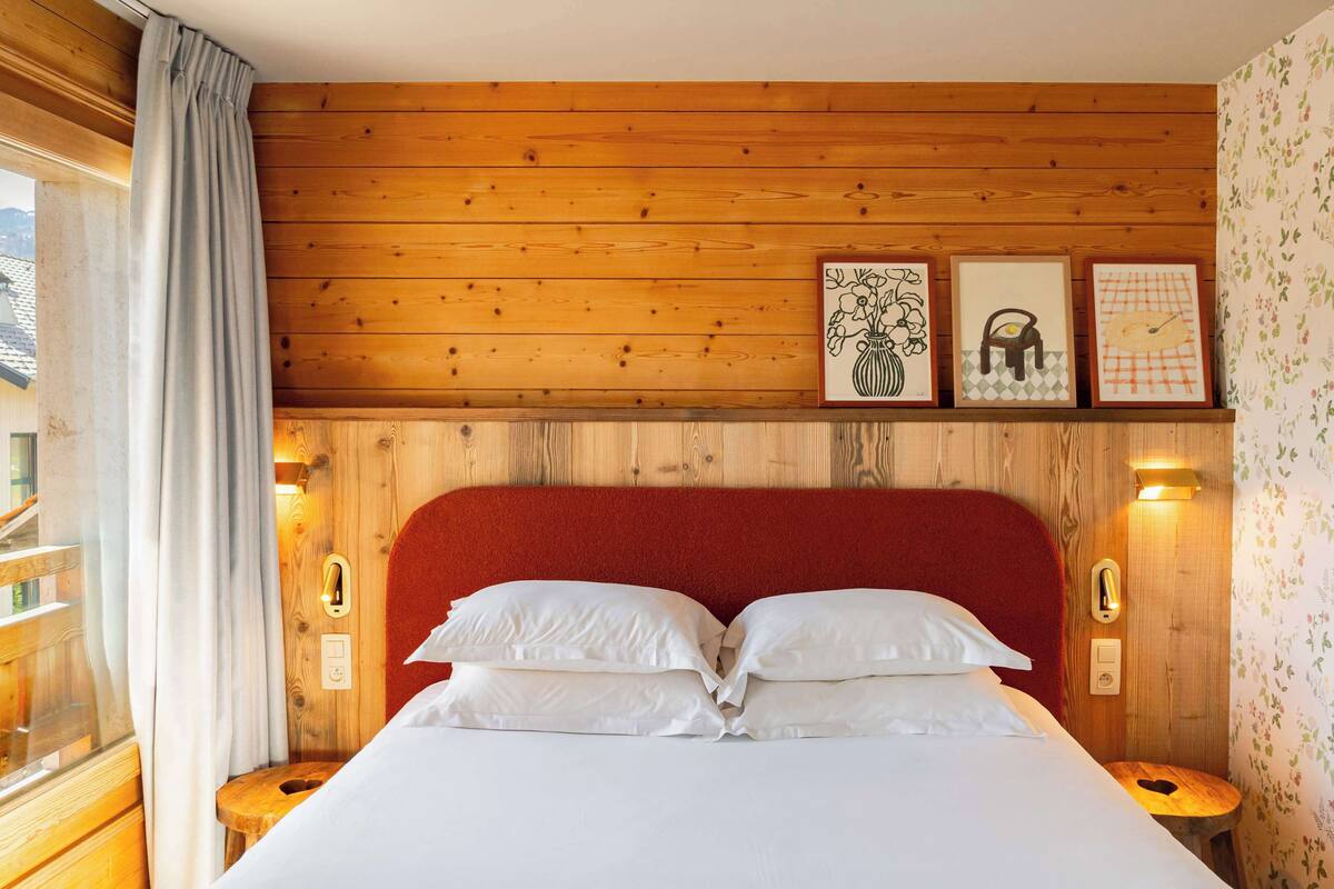 A wooden-paneled room with a bed, framed artwork, and a window with curtains.