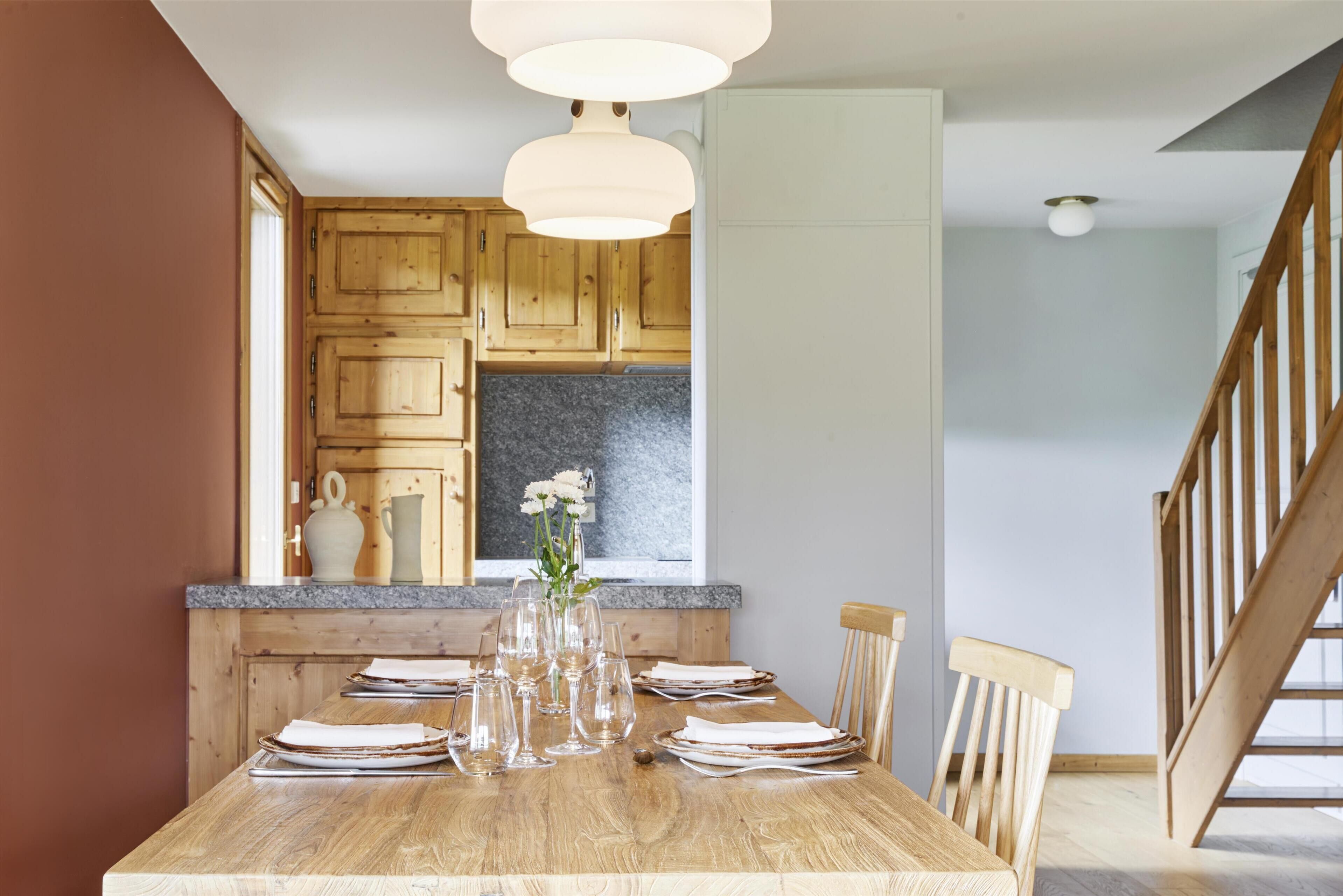 Un coin repas avec une table en bois dressée pour six personnes, un vase rempli de fleurs et, en arrière-plan, des meubles en bois.