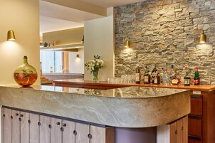 Zona de bar con pared de piedra, encimera de mármol y diversas botellas y vasos.
