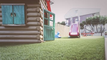 Un'area giochi per bambini con una casetta in legno, uno scivolo e una struttura per arrampicata.