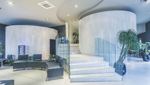 Un vestíbulo moderno con paredes curvas, una escalera, zona de estar y plantas en macetas.