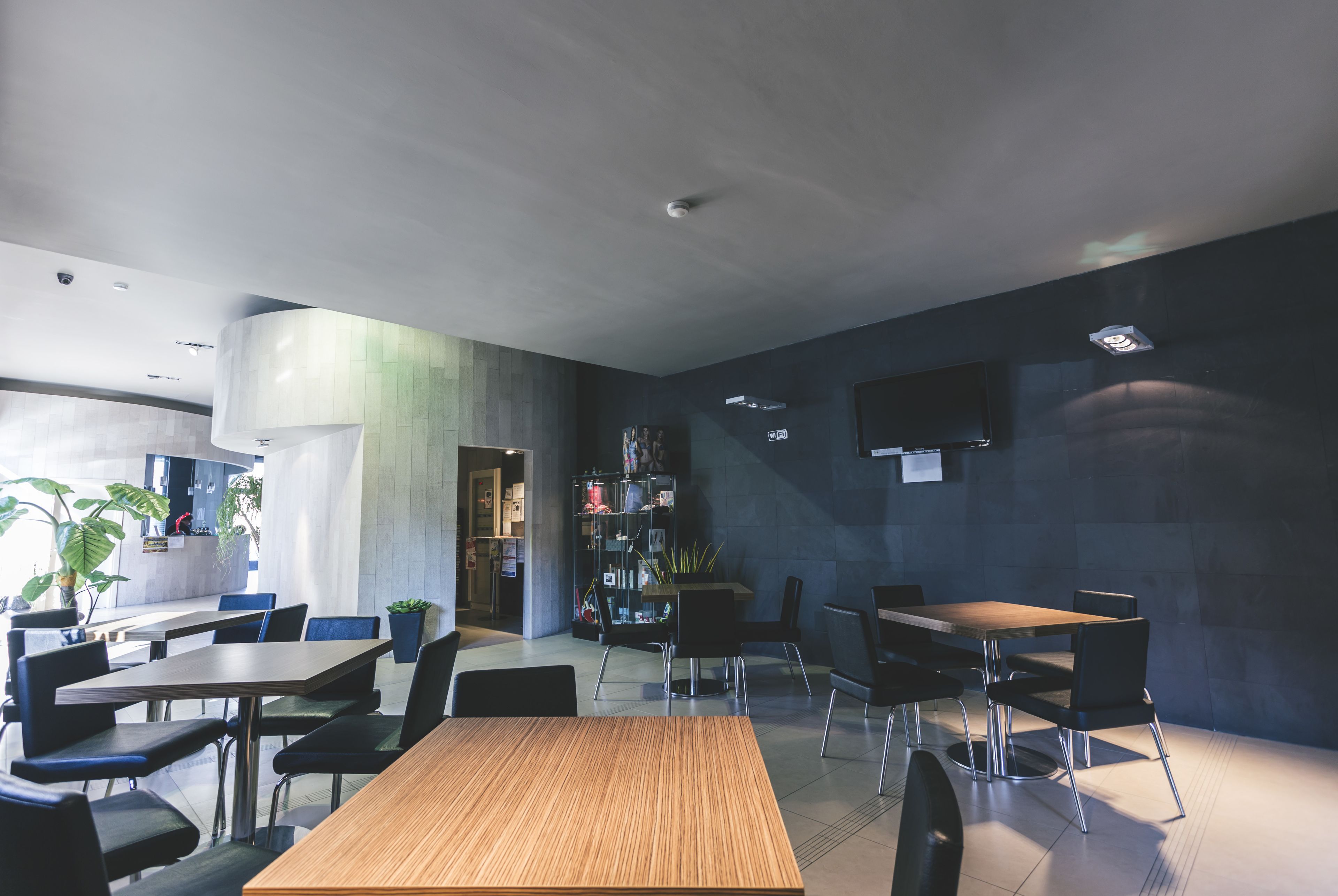 Una moderna zona pranzo con diversi tavoli e sedie, una cucina sullo sfondo e un televisore a schermo piatto montato al muro.