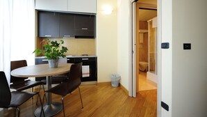 A modern kitchen with dark cabinets, a round dining table, and a potted plant. - Corvetto Residence (Milan)