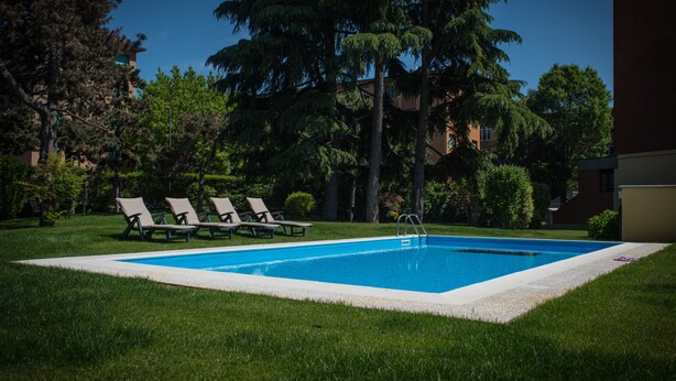 A rectangular swimming pool with a white edge, surrounded by a grassy area and trees. - Corvetto Residence (Milan)