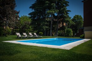A rectangular swimming pool with a white edge, surrounded by a grassy area and trees.