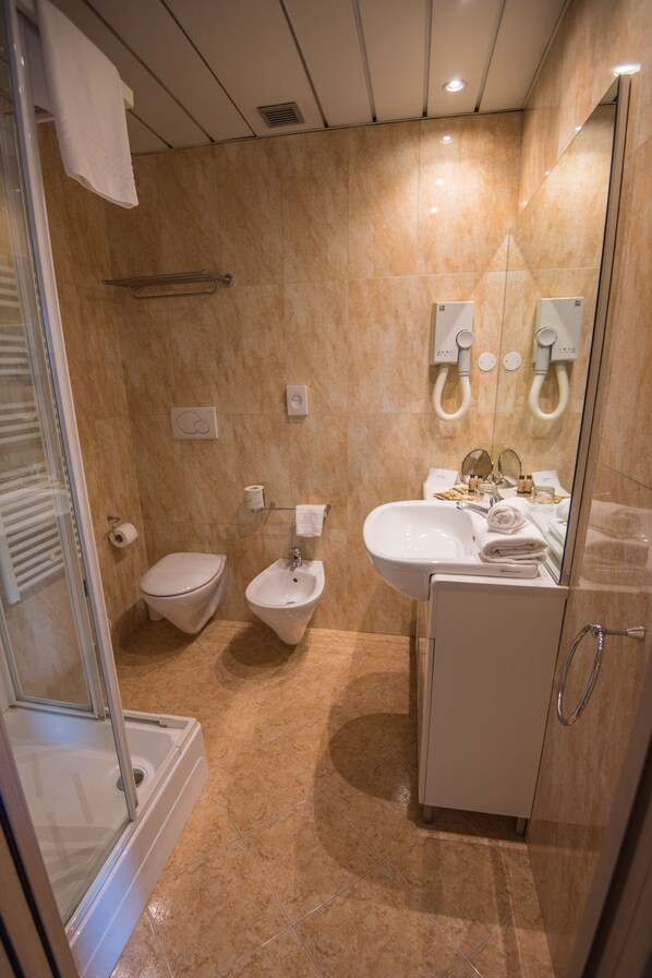 A modern bathroom with a glass shower enclosure, a toilet, bidet, and a sink with a mirror.