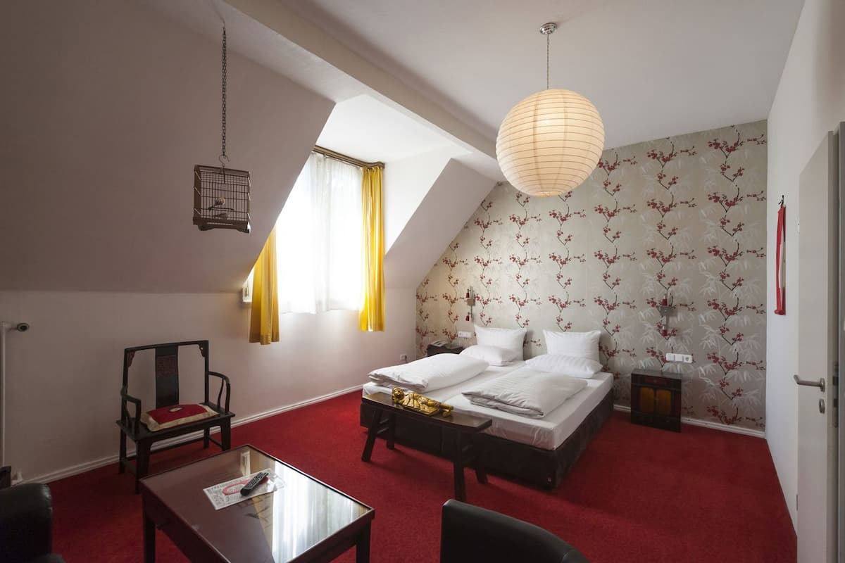 Ein Schlafzimmer mit einem Bett, einem Schreibtisch, einem Stuhl, einer Hängelampe und einem Fenster mit Vorhängen.