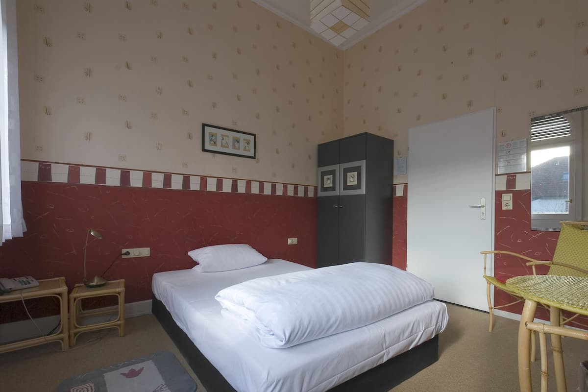 Ein Schlafzimmer mit Bett, Kleiderschrank, Schreibtisch mit Lampe und Stuhl.