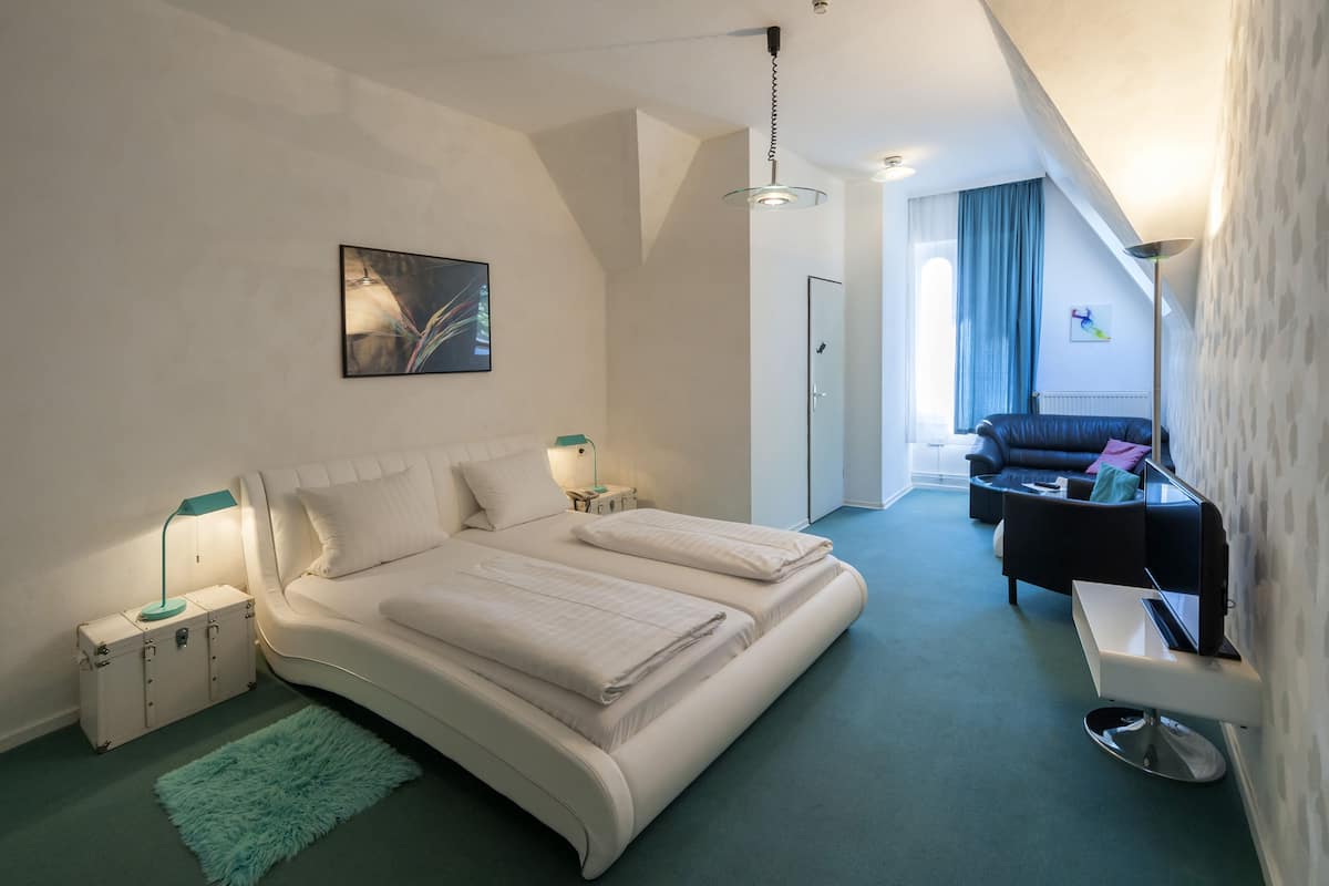 Ein modernes Schlafzimmer mit einem großen Bett, Nachttischen, einem Koffer und einem grünen Teppich.