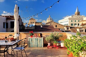 A rooftop terrace with a table, chairs, potted plants, and a string of lights against a cityscape backdrop. - mok'house (Rome)