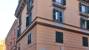 Un edificio de varios pisos con un estilo arquitectónico clásico, que cuenta con un balcón en el piso superior y una entrada a nivel de calle con una reja de metal.