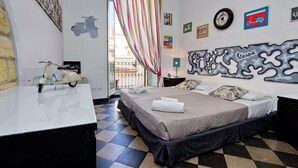 Habitación de hotel con cama, escritorio, una patineta, ventana con cortinas y decoración en la pared, incluyendo un mural de patineta y varias fotografías enmarcadas.