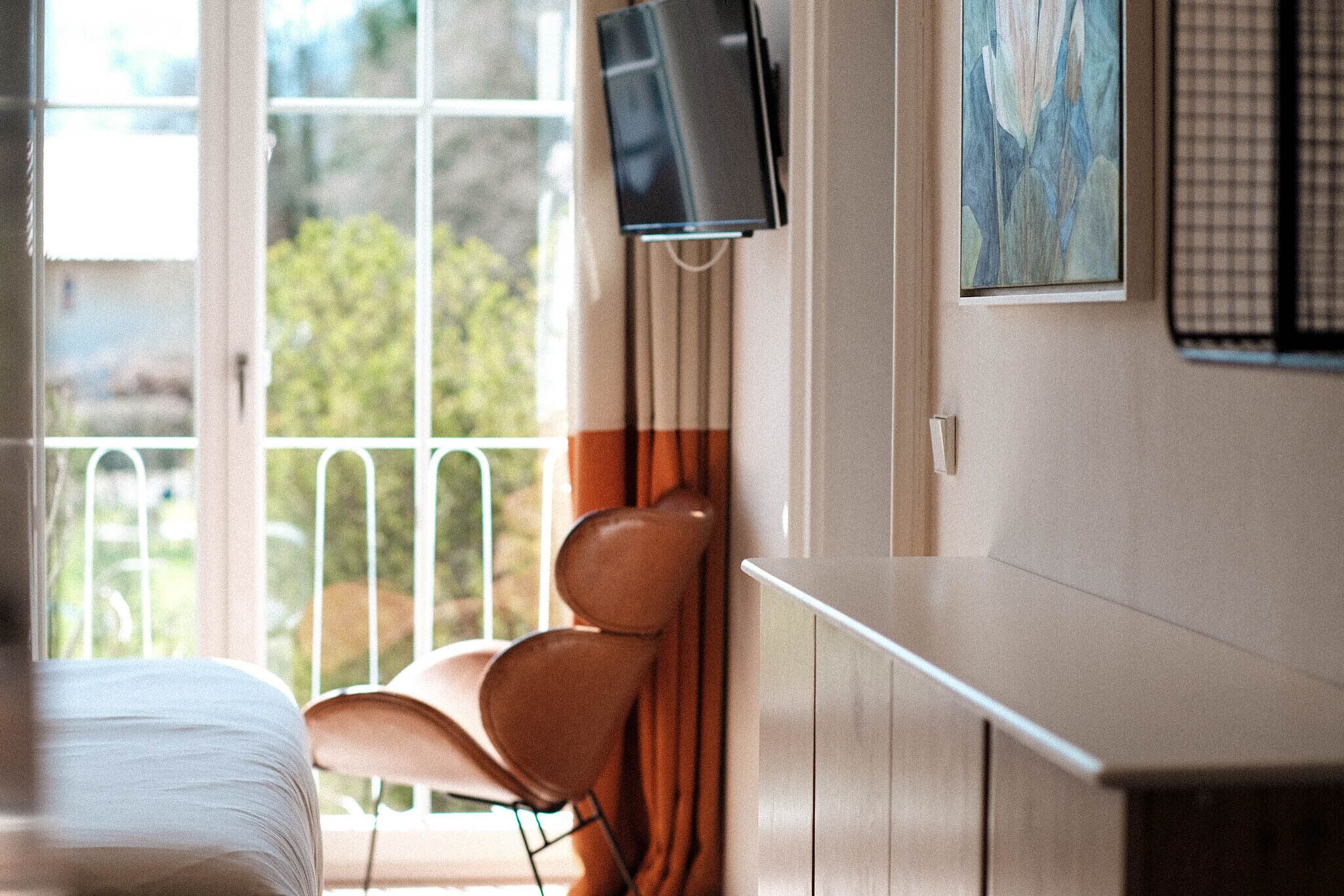 Habitación de hotel con cama, televisor en la pared, una silla y ventana con vistas a zonas verdes.