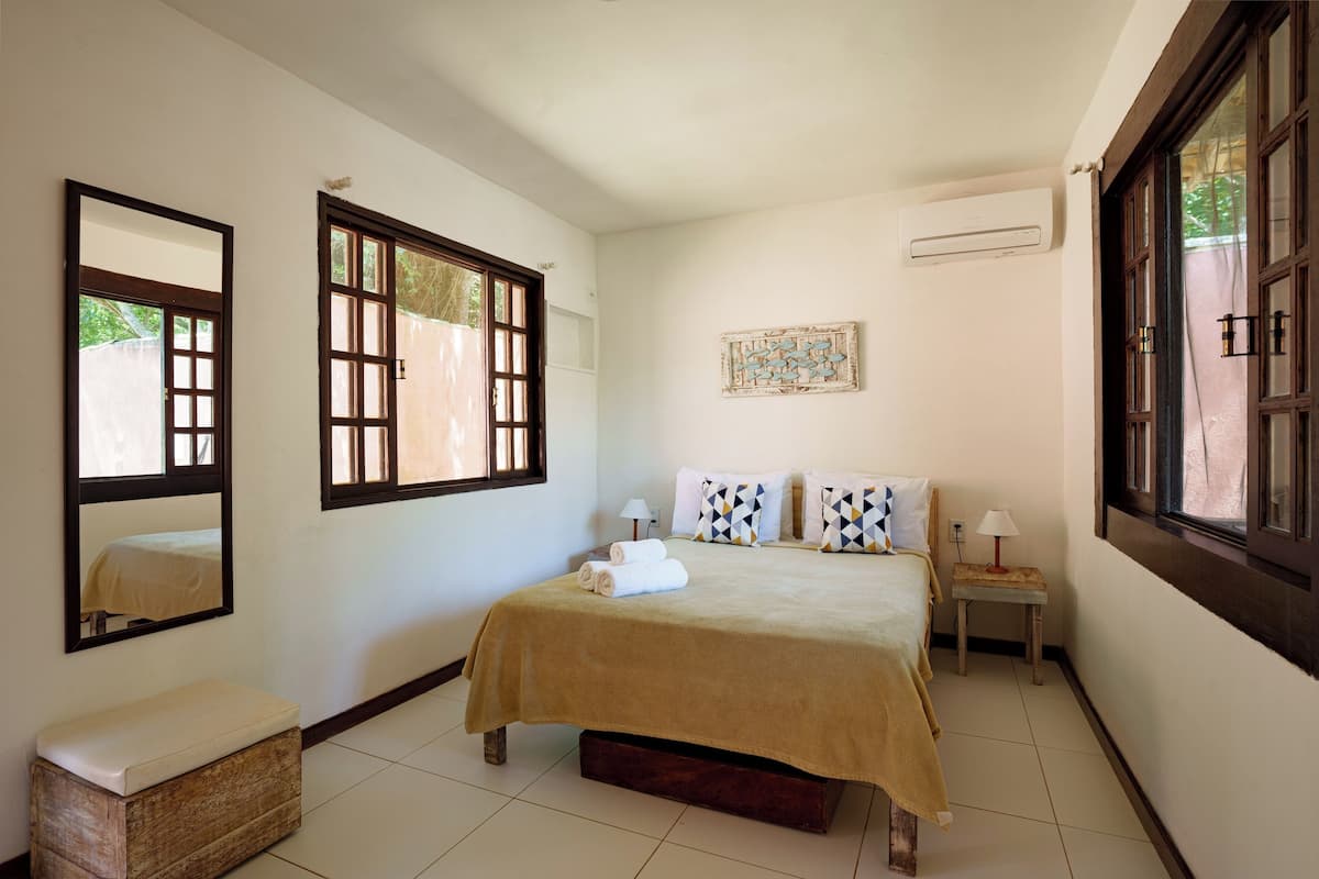 A bedroom with a bed, a bench, a nightstand, a lamp, and a window.