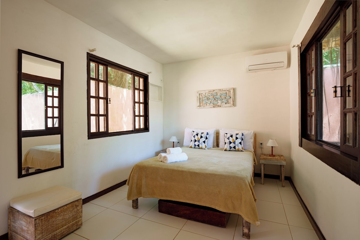 A bedroom with a bed, a bench, a nightstand, a lamp, and a window.