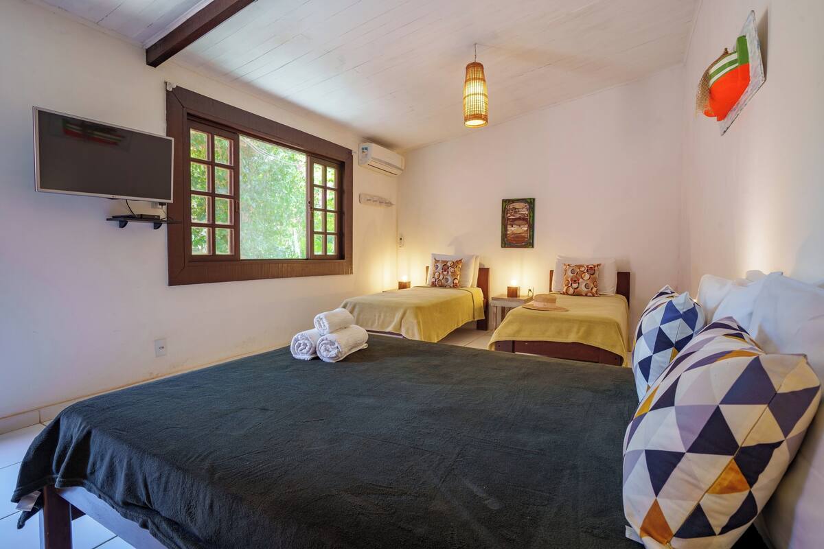 A room with two beds, a large window, and a TV mounted on the wall.