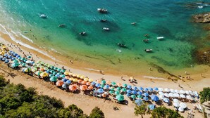 A beach with clear turquoise water, boats, and umbrellas. - Pousada Casa Cactus (Búzios)