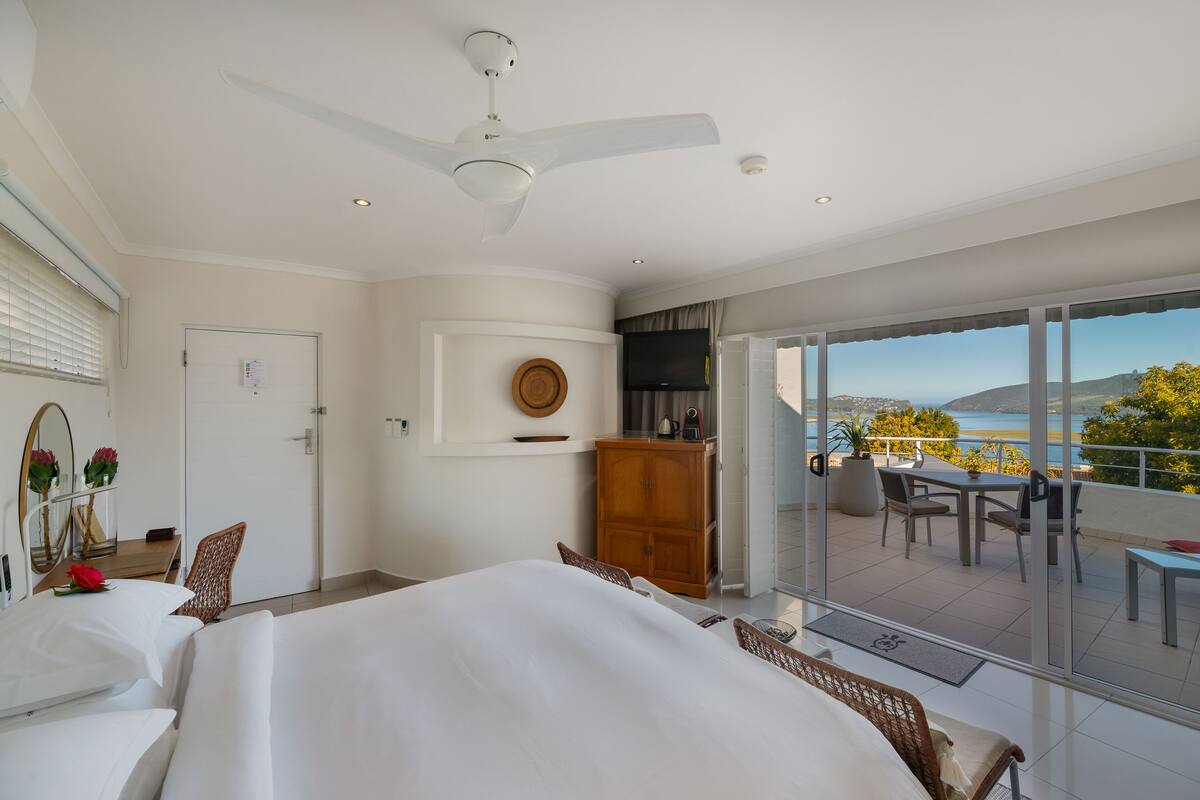 Une chambre d’hôtel équipée d’un lit, d’un bureau, d’une chaise, d’une armoire, d’une télévision et d’un balcon avec vue sur la mer.