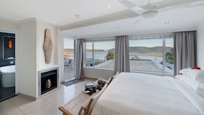 Une chambre d’hôtel moderne dotée d’un grand lit, d’un coin salon, d’une cheminée et offrant une vue sur la mer.