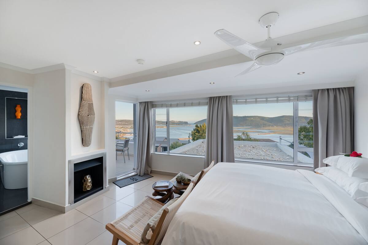 Une chambre d’hôtel moderne dotée d’un grand lit, d’un coin salon, d’une cheminée et offrant une vue sur la mer.