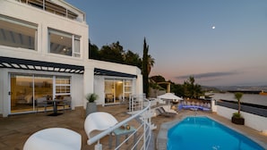 Un espace piscine extérieur moderne, offrant une vue dégagée sur la piscine, des chaises longues et une terrasse dotée d’une balustrade.
