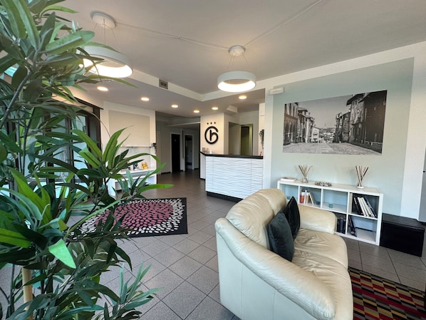 A modern reception area with a reception desk, a large framed photo on the wall, a leather sofa, and a potted plant.