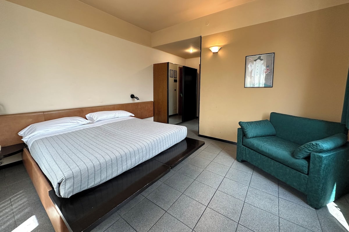 Ein Hotelzimmer mit einem Bett, einem grünen Sofa, einem Kleiderschrank und einem Spiegel.