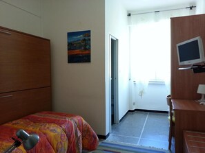 Une chambre d’hôtel avec un lit, un bureau avec un ordinateur, un tableau au mur et une fenêtre avec des rideaux.