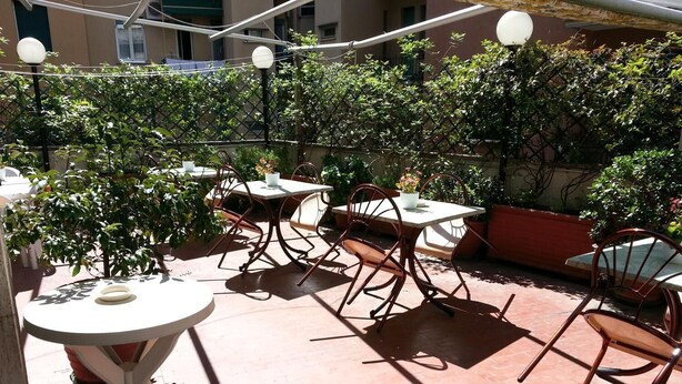 Un patio al aire libre con mesas y sillas, rodeado de follaje y un piso de ladrillo.