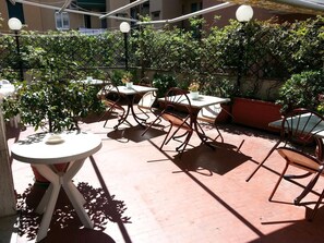 Un patio al aire libre con mesas y sillas, rodeado de follaje y un piso de ladrillo.