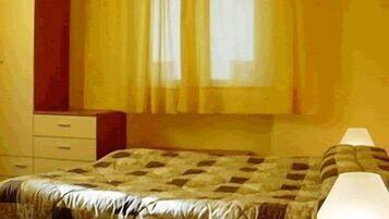 Ein Zimmer mit einem Bett, einem Nachttisch, einer Lampe und einem Fenster mit Vorhängen.