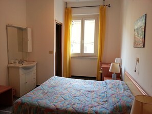 Une chambre à coucher comprenant un lit, une table de chevet, une lampe, une fenêtre avec des rideaux, un miroir et un lavabo.
