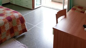 Una habitación con una cama, un escritorio de madera, un armario y un ventanal corredero que da a un espacio exterior.