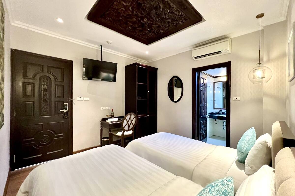 A hotel room with two beds, a desk with a chair, a TV mounted on the wall, a mirror, and an air conditioning unit.