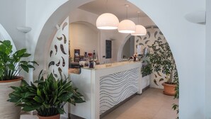 A modern hotel lobby with a reception desk, potted plants, and a large arched doorway. - Hotel Cala Reale (Stintino)