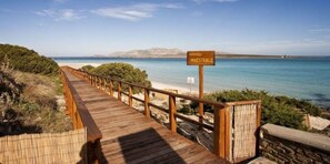 A wooden boardwalk leading to a beach with a sign reading "PAGERELLA MAESTRALE". - Hotel Cala Reale (Stintino)