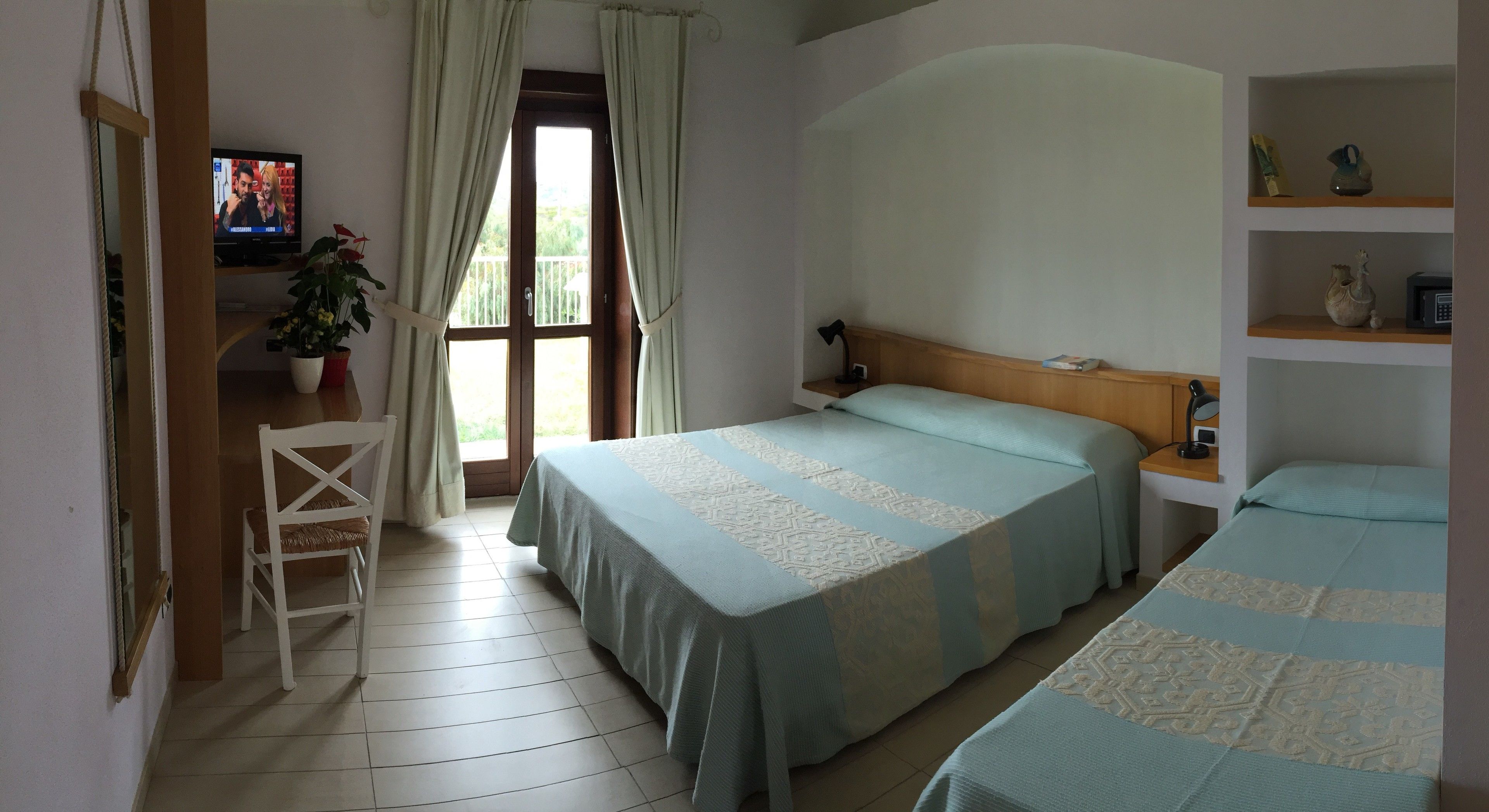 A hotel room with two beds, a television, a plant, and a window with curtains.