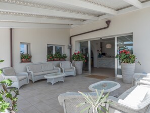A covered patio area with wicker furniture, potted plants, and a reception desk visible through a glass door. - Hotel Cala Reale (Stintino)
